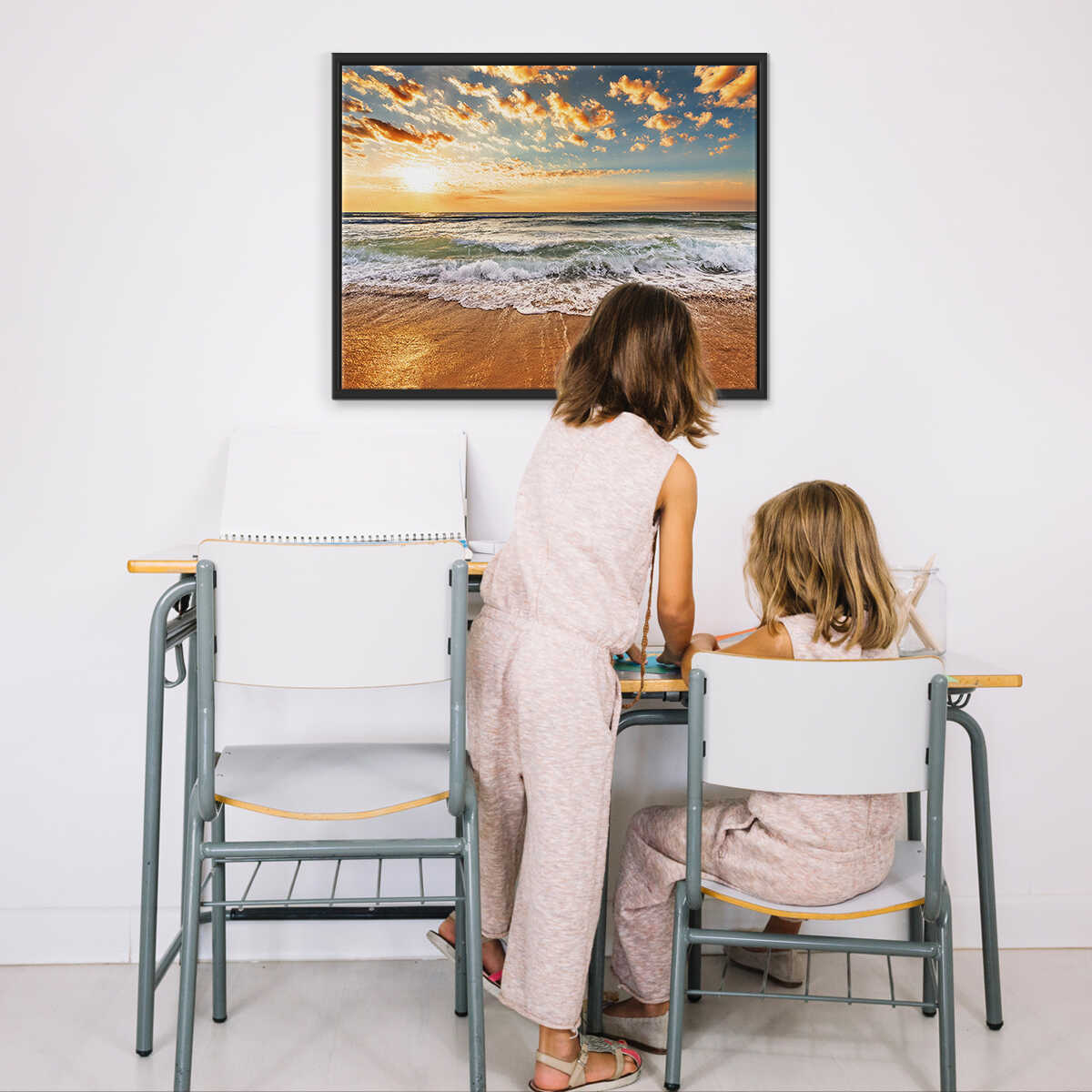 Childs sitting at a table with a framed beach scene on the wall.